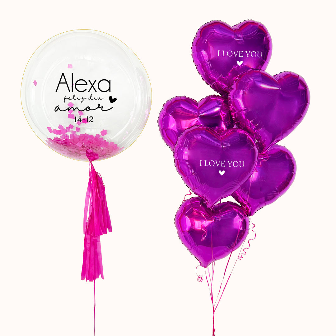 Ramo de globos compuesto por un globo burbuja con papel seda en su interior, decorada con 2 flequillos de papel, acompañado de 6 globos metálicos en forma de corazón color fucsia. 2 de ellos personalizados. Regalo para desear un Feliz Día en San Valentín o cualquier ocasión especial de aniversario o cumpleaños