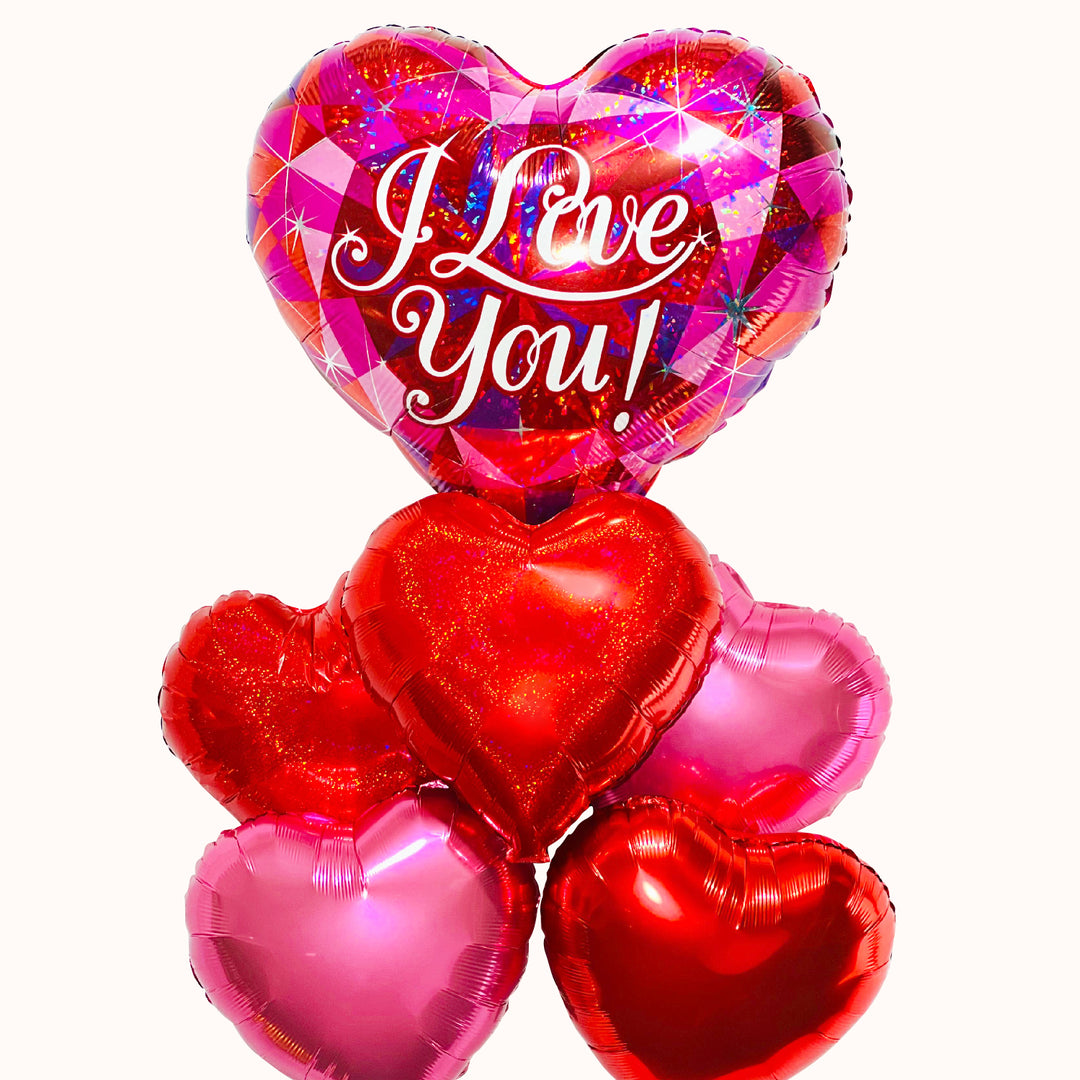 Arreglo de globos de helio: Bouquet de globos metálicos inflados con helio, que incluye un globo grande en tonos rosado, fucsia y rojo, impreso con la frase 'I Love You', acompañado de 3 globos en forma de corazón rojo y 2 globos en forma de corazón rosado. Regalo o detalle para San Valentín y aniversarios romanticos.