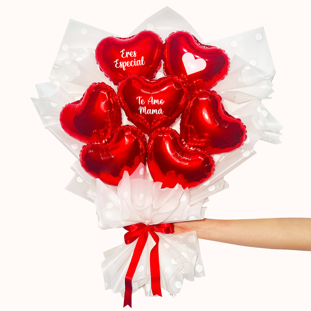 Ramo de globos metálicos en forma de corazón color rojo con mensajes en español 'Te Amo mamá', 'Eres Especial', envuelto en papel coreano decorativo blanco con lazo.