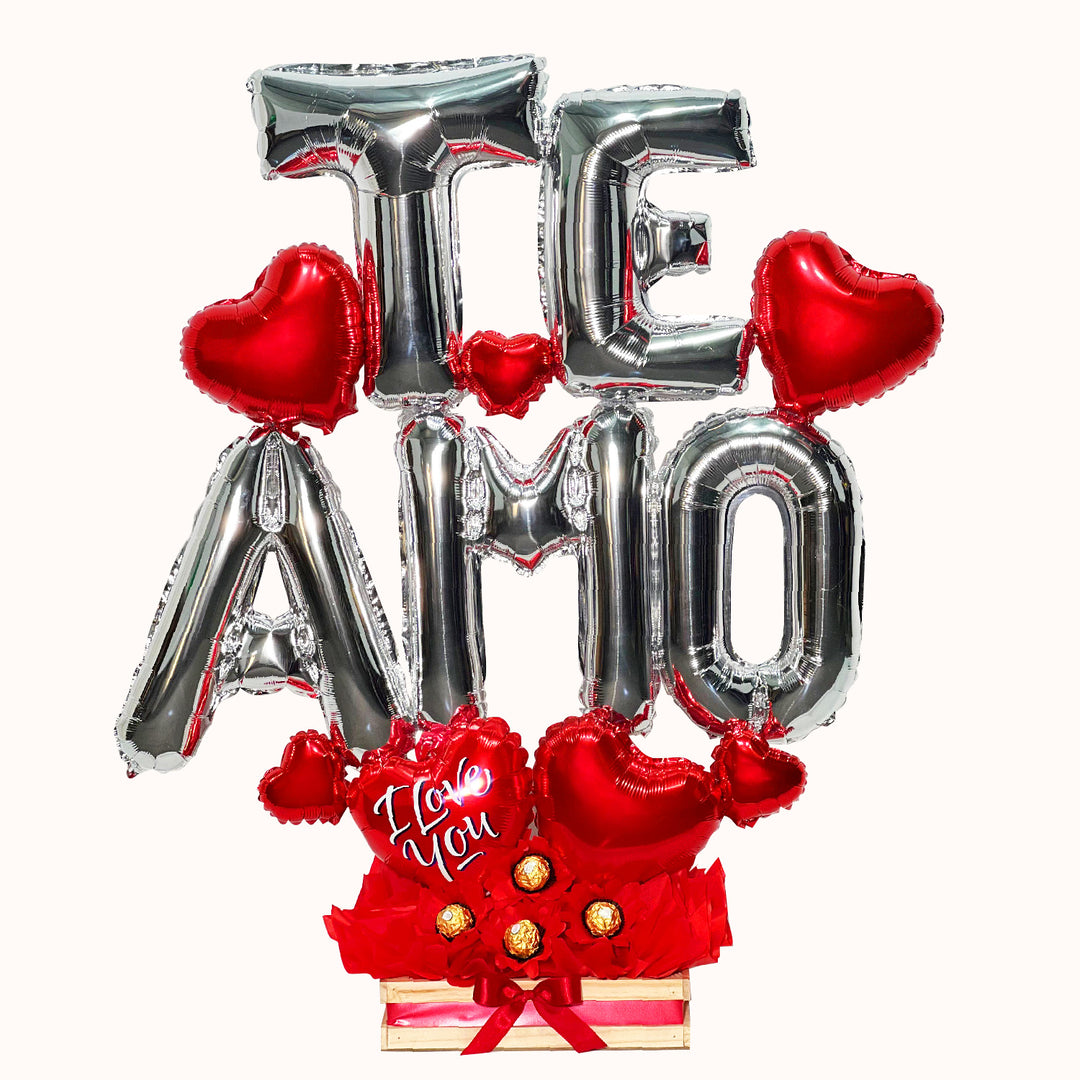 Gift box que incluye 5 letras metálicas plateadas formando la palabra 'TE AMO', 4 chocolates Ferrero Rocher, globitos decorativos y una caja de regalo pequeña. Medida 90 cm. Un detalle para regalo de San Valentín, el Día del Amor o en ocasión romántica.