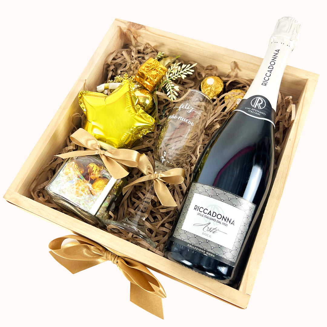 Hermoso gift box en base de madera que incluye Riunite Asti d’Oro 750 ml, 1 copa, 1 pomo de vidrio con chocolates y/o caramelos, 2 unidades de chocolate ferrero roche, adorno decorativo y globo, ideal para regalar con estilo y elegancia en Año Nuevo.