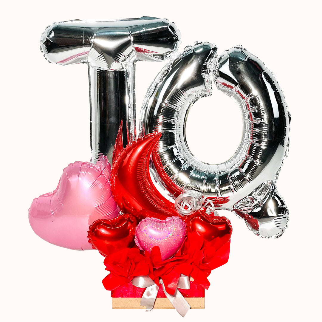 Gift box con globos de letras 'TQ', para regalo de enamorada, elaborado con globos metálicos en tonos plata, rosa y rojo.