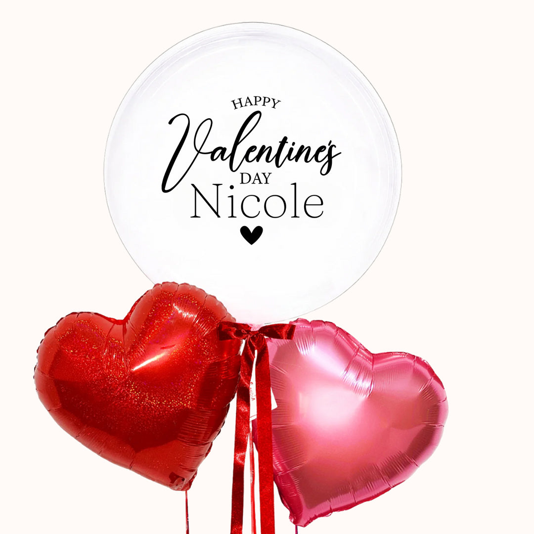 Bouquet de globos para celebrar el Día del Amor, que incluye un globo burbuja transparente personalizado con la frase “Happy Valentine’s Day”, acompañado de 2 globos metálicos en forma de corazón en tonos rojo y rosado.
