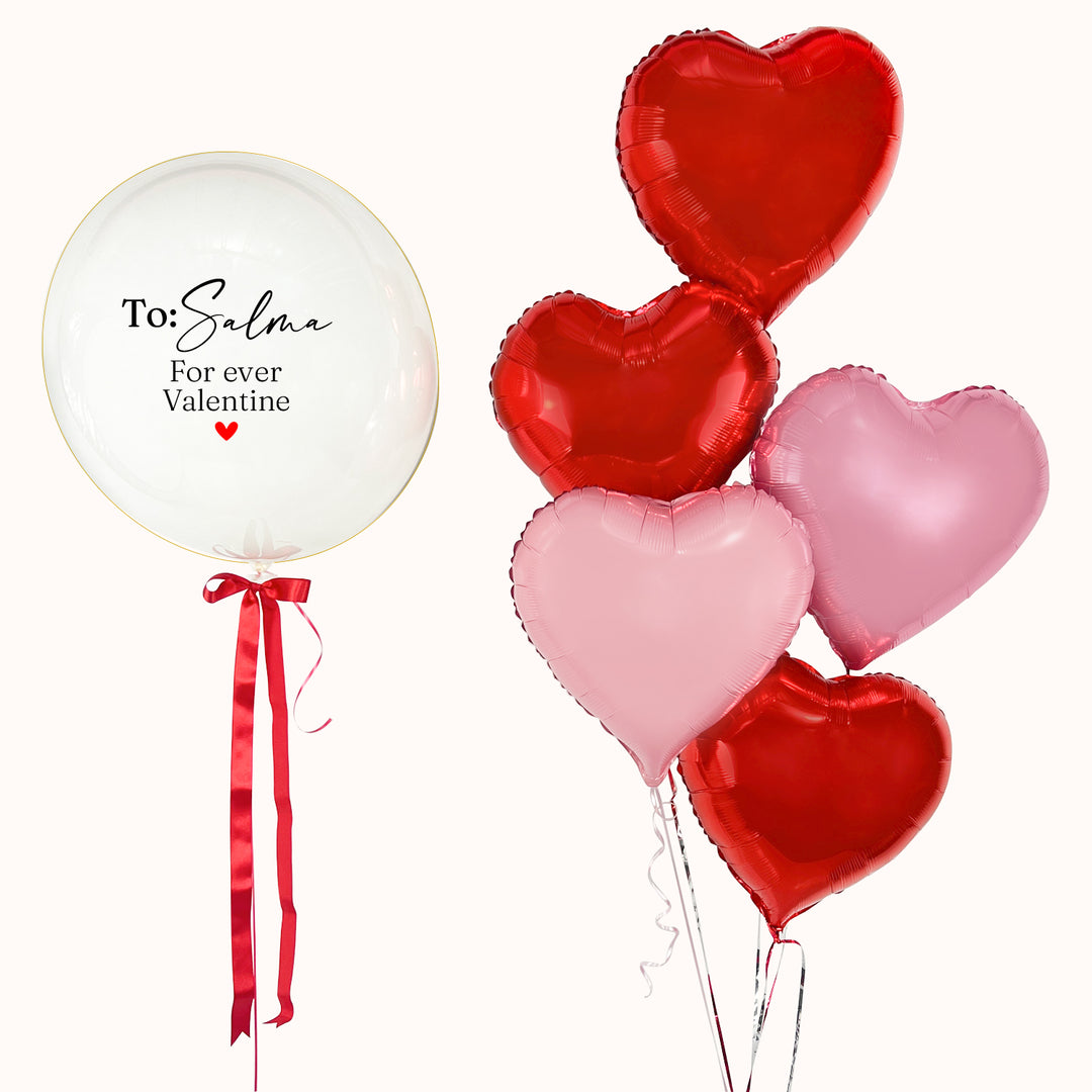 En San Valentín, regala un globo burbuja con globo interno, personalizado, acompañado de 5 globos en forma de corazón en tonos rojo y rosado. Un detalle para expresar tu amor. Inflado con helio puro.