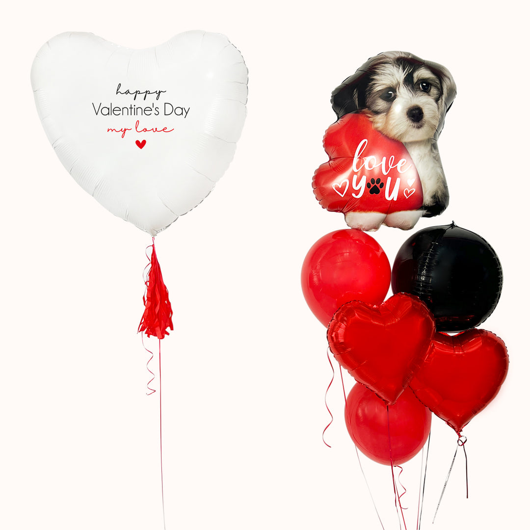 Bouquet para celebrar San Valentín. Regala amor con este corazón blanco personalizado, acompañado de un bouquet de globos que incluye 2 globos en forma de corazón, una esfera negra, 2 globos de látex rojos y un globo de perro con la frase “Love You”. Arreglo de globos para San Valentín.