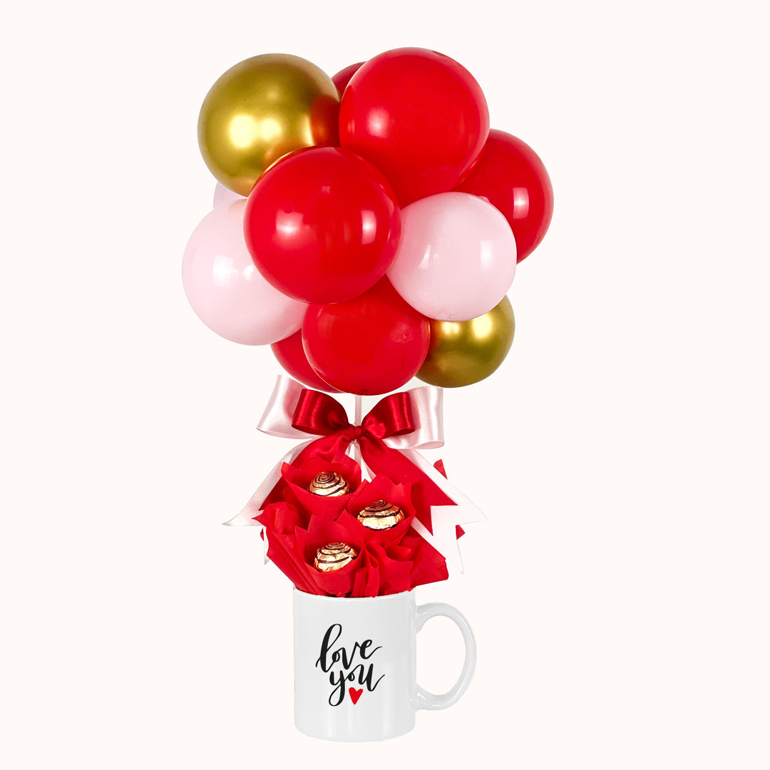 Regalo de amor con taza y chocolates tipo bombón y globo aerostático realizado con globitos látex en colores rojo, rosado y dorado. Regalo especial para San Valentín.